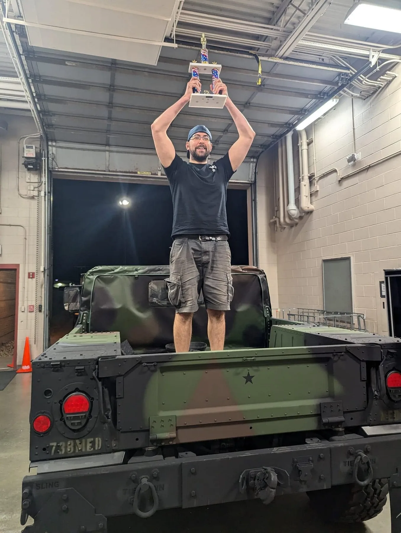 An attendee standing on the back of a military truck, holding a Red, White, and Clix trophy above his head.