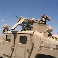Wesley Robertson in desert uniform, sitting on top of a Humvee with his feet up on the mounted gun.
