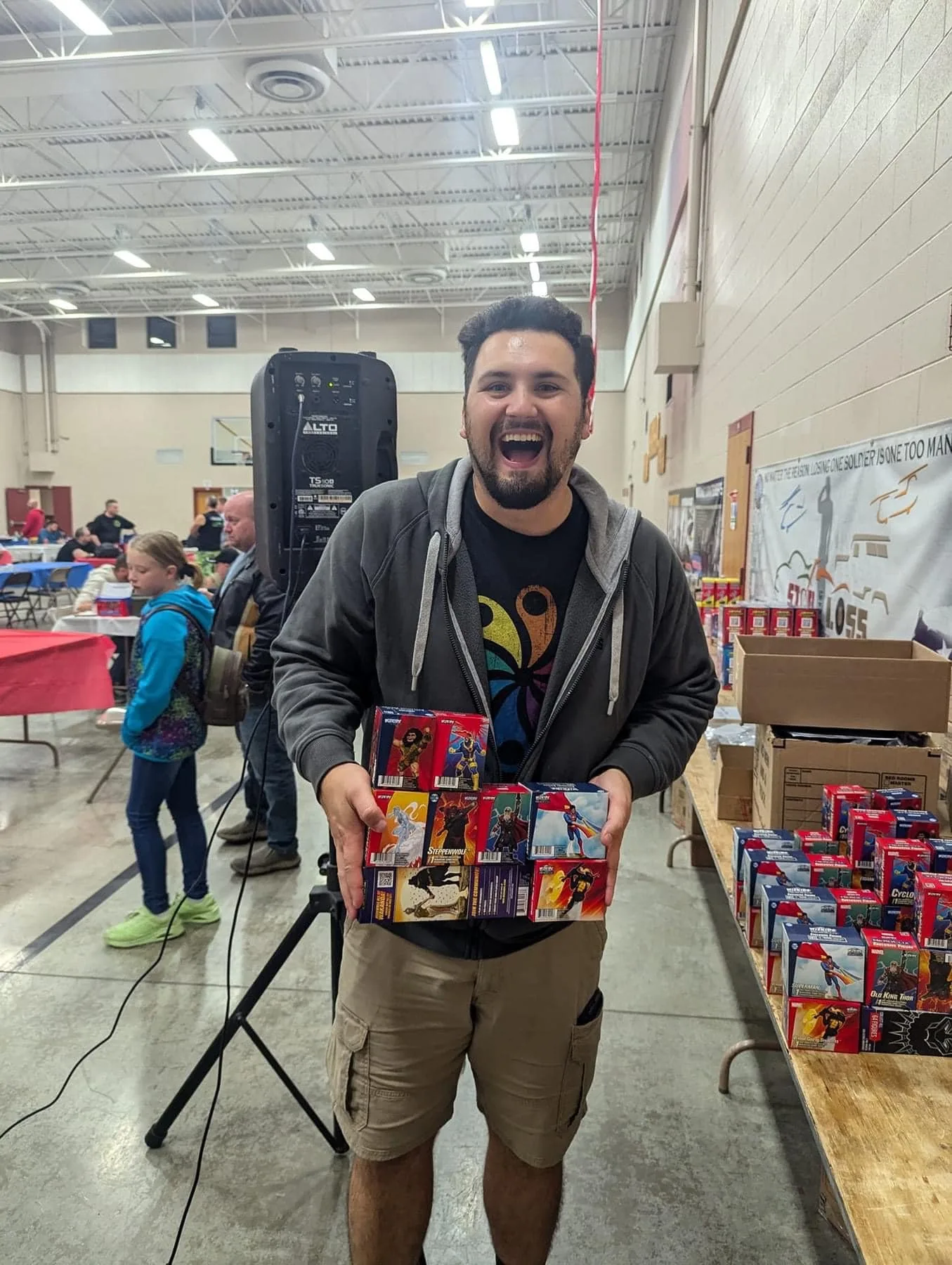 A grinning attendee holding a box packed with HeroClix prize boosters.